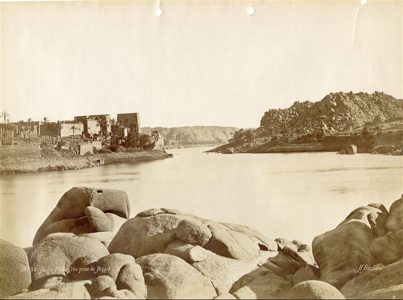 The image shows a view from the north-west of the temple complex  of Isis on the island of Philae, photographed from the neighbouring island of Bigeh. The author's signature can be found at the bottom right.