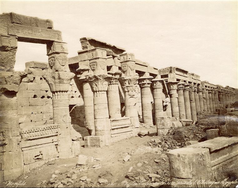 The image shows a view of the long western colonnade of the temple complex of Isis at Philae seen from the south, where at the end, the Hathoric capitals of the Kiosk of Pharaoh Nectanebo I can be seen on the left. The author's signature can be found at the bottom left. 