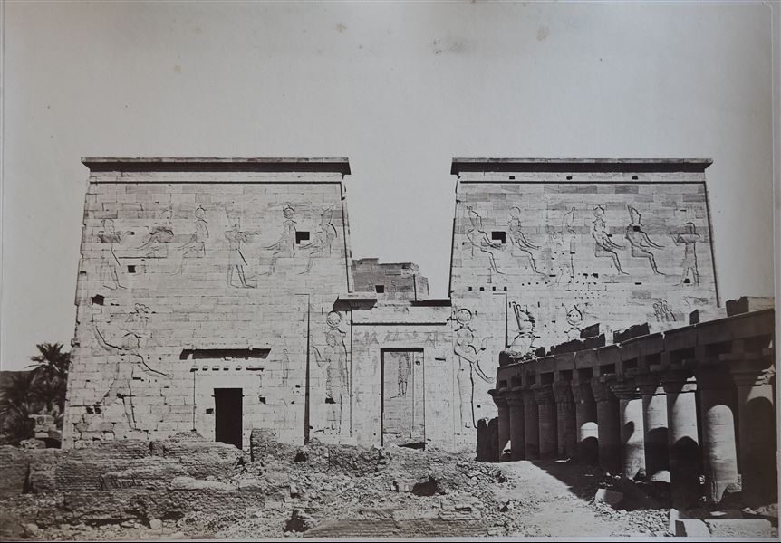 The photograph shows the first pylon and the colonnaded courtyard in front of it, from the Temple of Isis on the island of Philae. Note the presence of small brick buildings from a later period, built on a surface that still covers the lower part of the ancient columns. 