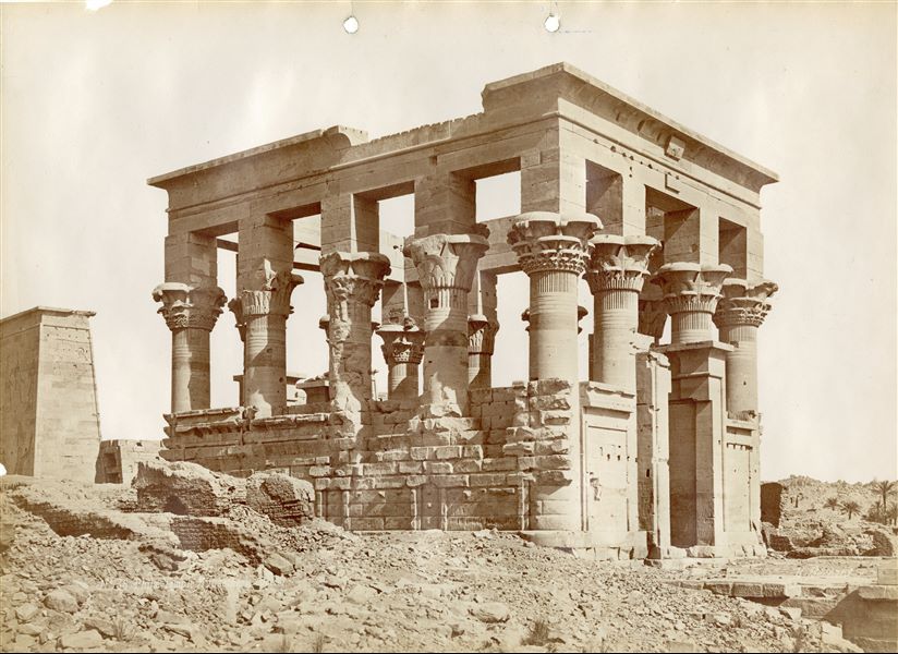The picture shows Trajan's Kiosk (north and west sides), still in its original position, and some Coptic mud-brick structures no longer visible after the temple was moved and rebuilt on the Agilkia island. On the left, a pylon from the temple of Isis is can be seen. The temple was relocated in the 1970s to the nearby island of Agilkia, following the construction of the Aswan Dam and the formation of Lake Nasser, which would have submerged it.  