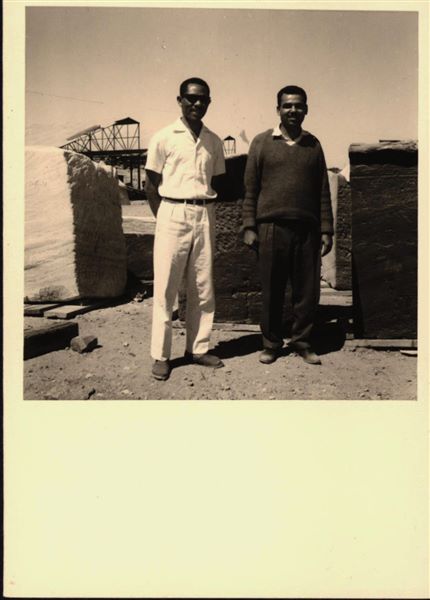 Storage at Wadi es-Sebua, where rock-cut chapel of Ellesiya blocks were kept for a short time. Here they are arranged in rows waiting to be transferred to Turin after the United Arab Republic decided to gift the rock-cut chapel to the Italian Republic. Photographed in the foreground, two inspectors from the Egyptian Antiquities Service. 
