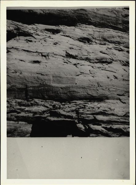 Photograph of the rock-cut rock-cut chapel of Ellesiya in its original location within the Nubian landscape. In addition to the mountain (in which the rock-cut chapel was carved), the Nile River can be seen in the foreground, which shortly afterwards, would begin to rise until it submerged the rock-cut chapel, due to the construction of the Aswan Dam. 