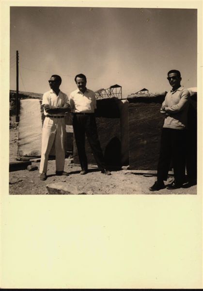 Storage at Wadi es-Sebua, where the rock-cut chapel of Ellesiya blocks were kept for a short time. Here they are arranged in rows waiting to be transferred to Turin after the United Arab Republic decided to gift the rock-cut chapel to the Italian Republic. Standing in the foreground, two inspectors from the Egyptian Antiquities Service, and in the centre, Silvio Curto, who was the representative of Museo Egizio at the time.