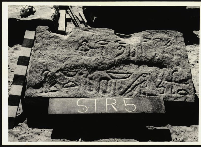 Storage at Wadi es-Sebua, one of the 66 blocks from the rock-cut chapel of Ellesiya stored waiting to be transported to Turin, after the United Arab Republic decided to gift the rock-cut chapel to the Italian Republic. One of the blocks forming part of the right side of the recess, on the rock-cut chapel's exterior façade. 

