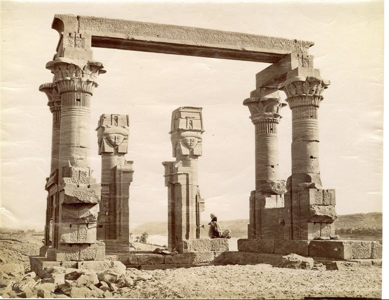 Veduta dei resti del chiosco di Età Romana (III sec. d.C.) nel tempio di Iside a Qertassi, in Nubia, nella sua posizione originaria. Un abitante locale è seduto sul basamento di una colonna con capitello hathorico. Il tempio fu spostato in seguito alla costruzione della diga di Assuan e alla formazione del lago Nasser, che lo avrebbe sommerso, e ri-eretto nel 1963 nei pressi di Nuova Kalabsha, un’altura poco distante da Assuan. In basso a sinistra, la firma dell’autore. 