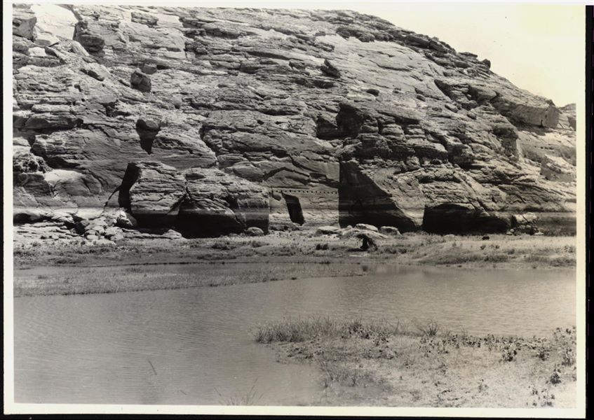 Fotografia del tempio rupestre di Ellesiya nel suo luogo originale, all’interno del paesaggio Nubiano. Oltre alla montagna, nella quale il tempio fu scavato, si vede la presenza del fiume Nilo, che dopo poco tempo, a causa della costruzione della diga di Assuan, avrebbe iniziato a crescere fino a sommergere il tempio.