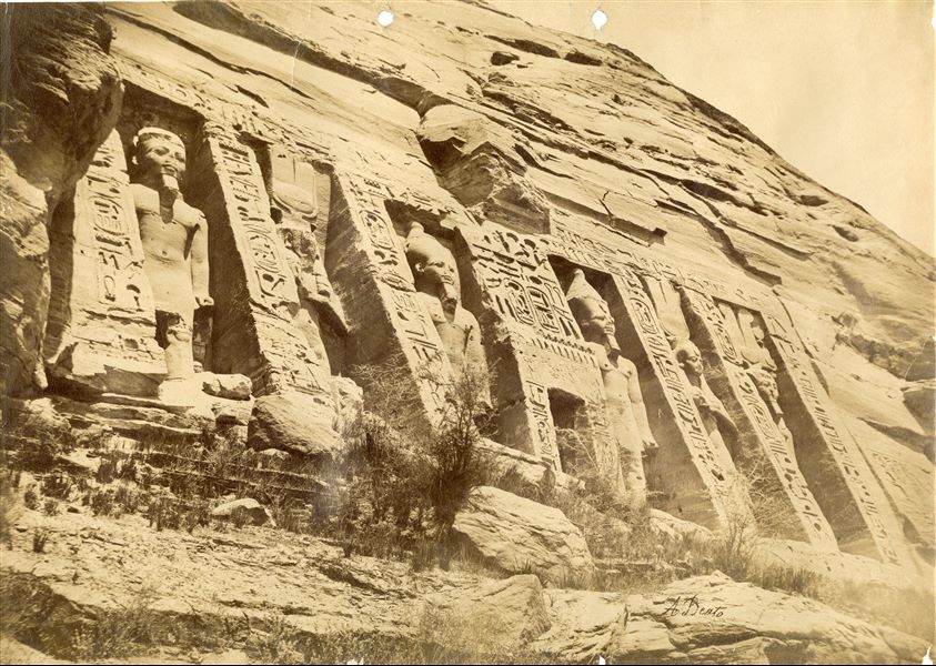 View of the façade of the Small Temple of Abu Simbel, with the colossal statues depicting the deified Pharaoh Ramesses II and Queen Nefertari. In the 1960s this temple, together with the Great Temple, were moved and placed on higher ground, as they were threatened by the rising waters of Lake Nasser following the construction of the Aswan Dam. Below, the signature of the author. 