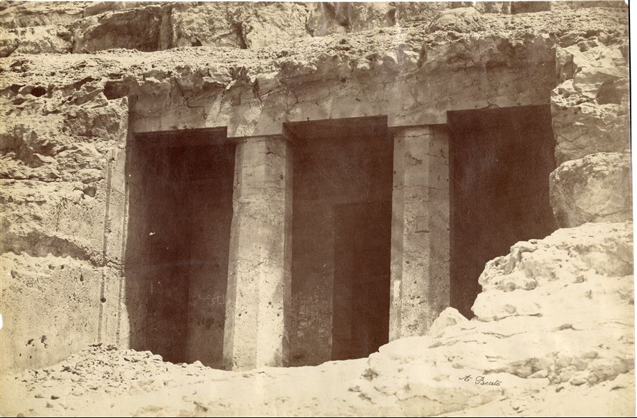 La fotografia mostra l'accesso alla tomba rupestre (n° 2) del governatore Amenemhat detto Ameny, nella necropoli di Beni Hasan. La firma dell’autore è posta in basso a destra.