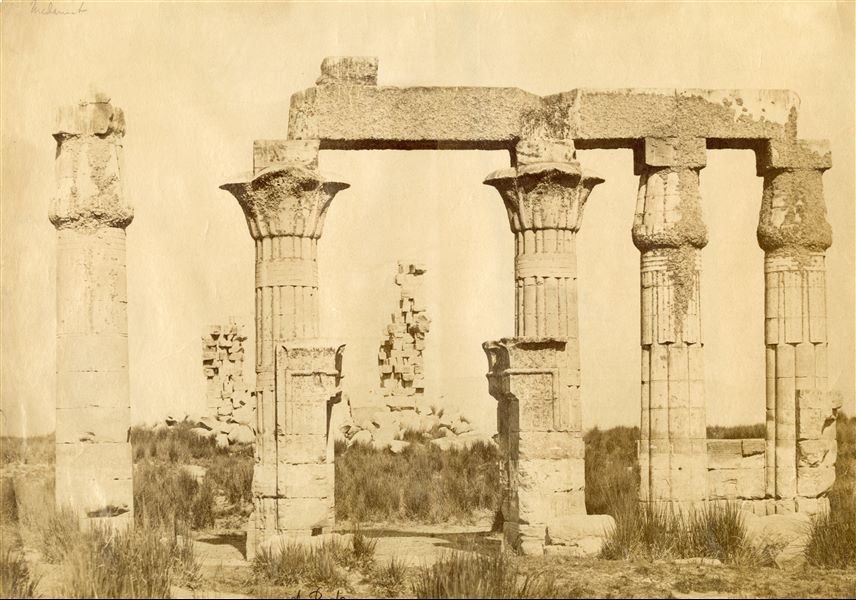 La fotografia propone la veduta da sud-est delle rovine dell'atrio colonnato del tempio di Montu costruito durante il regno del faraone Tolemeo VIII Evergete II a Nag' el-Madamud, nel II secolo a.C. . La firma dell’autore si trova in basso.