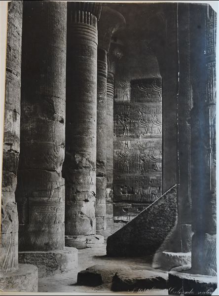 La fotografia rappresenta alcune colonne nella sala Ipostila del tempio di Khnum, costruito in Età Romana, a Esna. Da notare la presenza di una scalinata, oggi rimossa. La firma dell’autore è posta in basso a sinistra. 