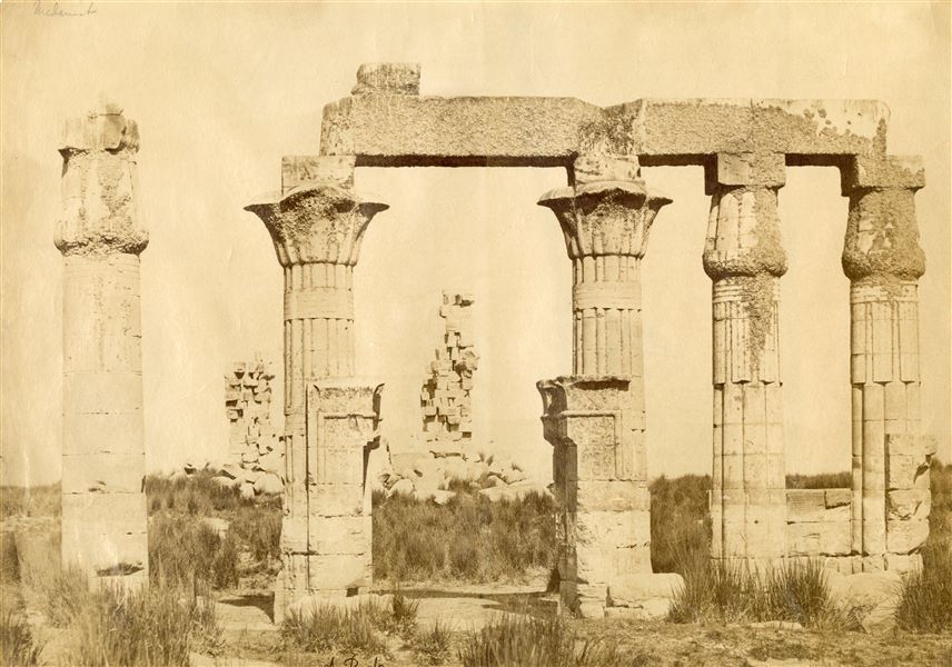 The photograph shows a view from the south-east of the ruins of the colonnaded hall from the Temple of Montu built during the reign of Pharaoh Ptolemy VIII Euergetes II at Nag' el-Madamud in the 2nd century BCE. The author's signature can be found at the bottom. 