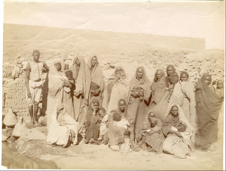 Fotografia di gruppo in Nubia, con alcune donne, i loro figli e un uomo. In basso a sinistra si trova la firma dell’autore.