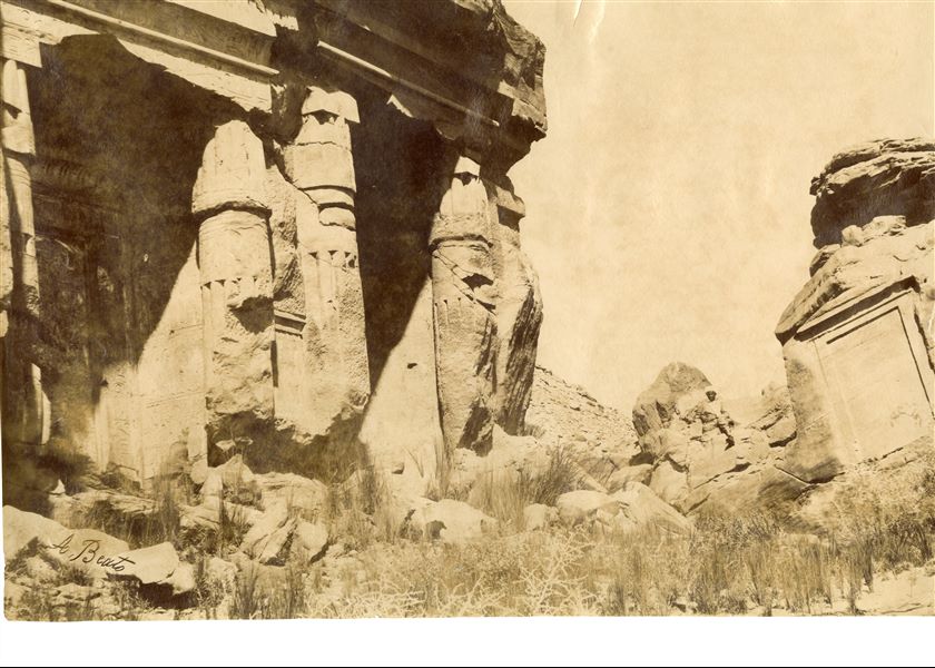 La foto ritrae una prospettiva delle cappelle rupestri presso Gebel Silsila costruite dai faraoni Ramesse II e Merenptah, tra le cui rovine siede un abitante del luogo. In basso a sinistra la firma dell’autore.