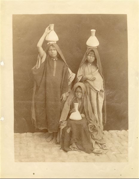 Photograph of three young female water carriers, posing for the photographer. 
