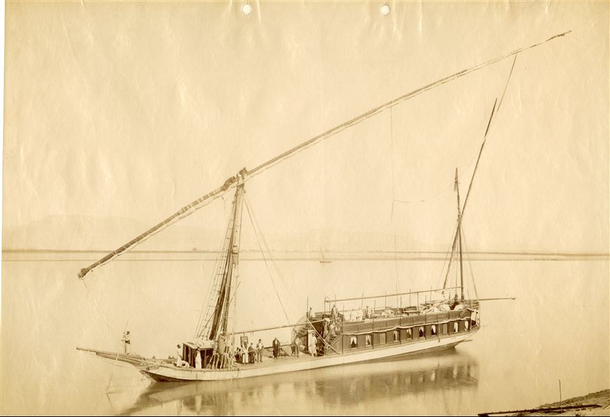 The image shows a cruise ship anchored on the Nile, with a group of tourists on the upper deck and service staff on the lower.