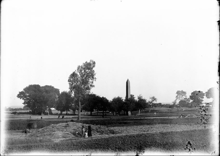 Area of the sacred enclosure, north and west sides of the obelisk of Sesostris I; a saqiyah is visible, from the north-east. In the foreground, we see cultivated fields. Schiaparelli excavations.
