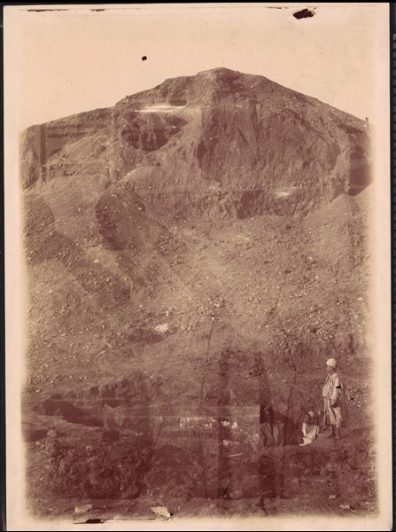 Granite blocks of a temple structure surfacing from the ground, during excavations by the Italian Archaeological Mission in Heliopolis. The photograph also features an overlay, showing a wall from Nefertari's tomb (QV66) in the Valley of the Queens. Schiaparelli excavations. 