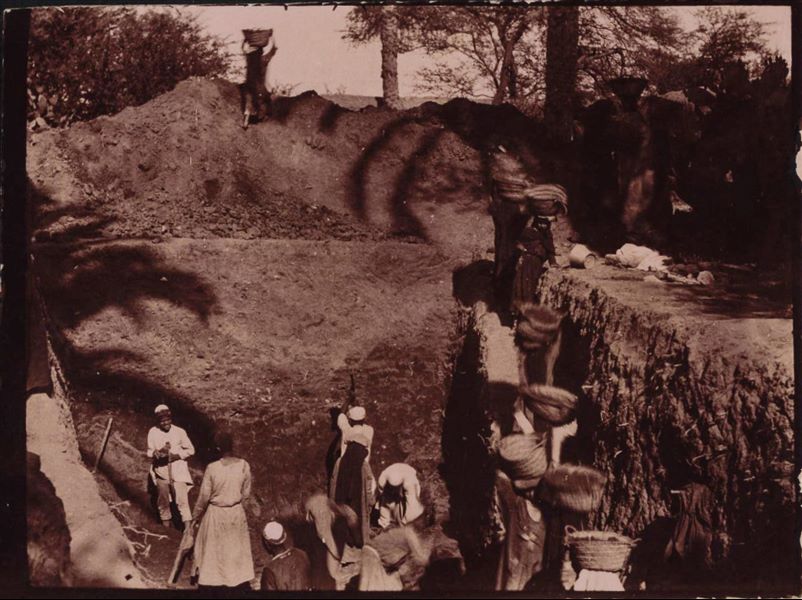 Large excavation trench next to a wall, which lies beyond the mound of loose earth. These are excavations possibly undertaken in the garden of Latif; he was an Egyptian man who owned a house and land in Heliopolis. Schiaparelli excavations.