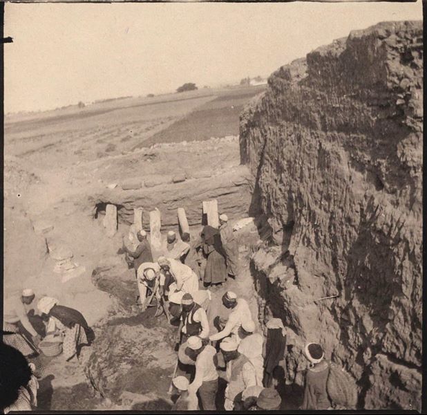 Area of the Sun Temple during excavations, next to abandoned structures with remains of Arabic houses. There are cultivated fields in the background. Behind the photographer, the obelisk of Sesostris I can be seen. Schiaparelli excavations.