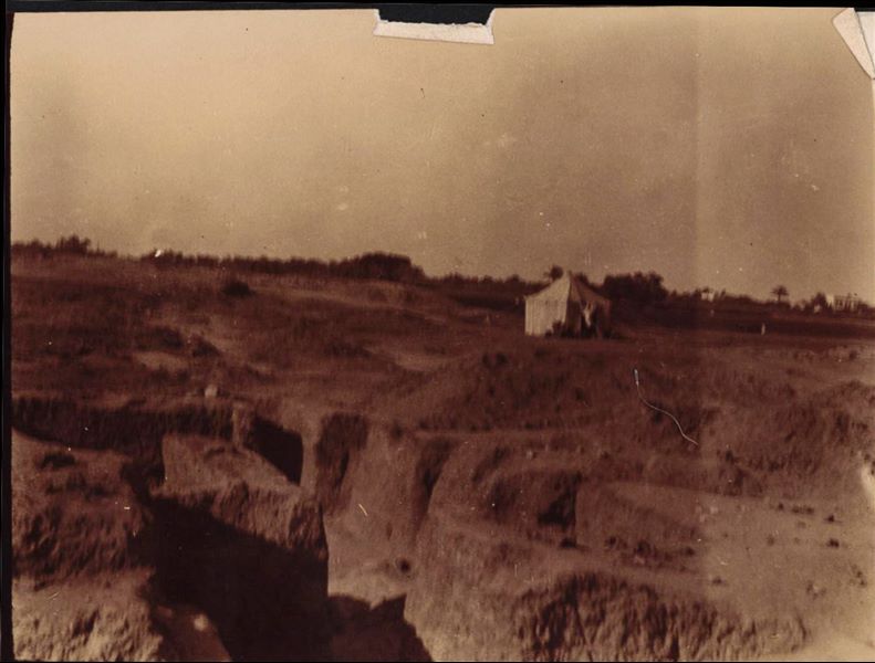 Excavation trenches in the Kom area. A white tent used by the Italian Archaeological Mission can be seen. In the background, to the right, there is a house. Schiaparelli excavations.