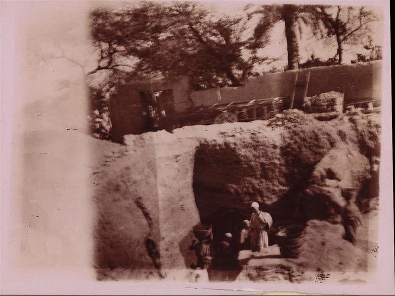Trincea di scavo nell’area del santuario del sole. Sullo sfondo si trova il muro della casa di Latif. Fotografia sovraesposta e realizzata a seppia. Scavi Schiaparelli.