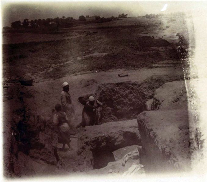Excavation trench in the Kom area, where a bridge structure can be seen. In the background there are the cultivated fields of Heliopolis, as well as a house and a vertical structure identifiable as the obelisk of Sesostris I. Schiaparelli excavations.