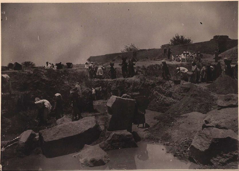 Temple of Mnevis, trench with fragments of the naos of Psamtik I. Note the muddy ground. This paper print has been toned with sepia.  Schiaparelli excavations.