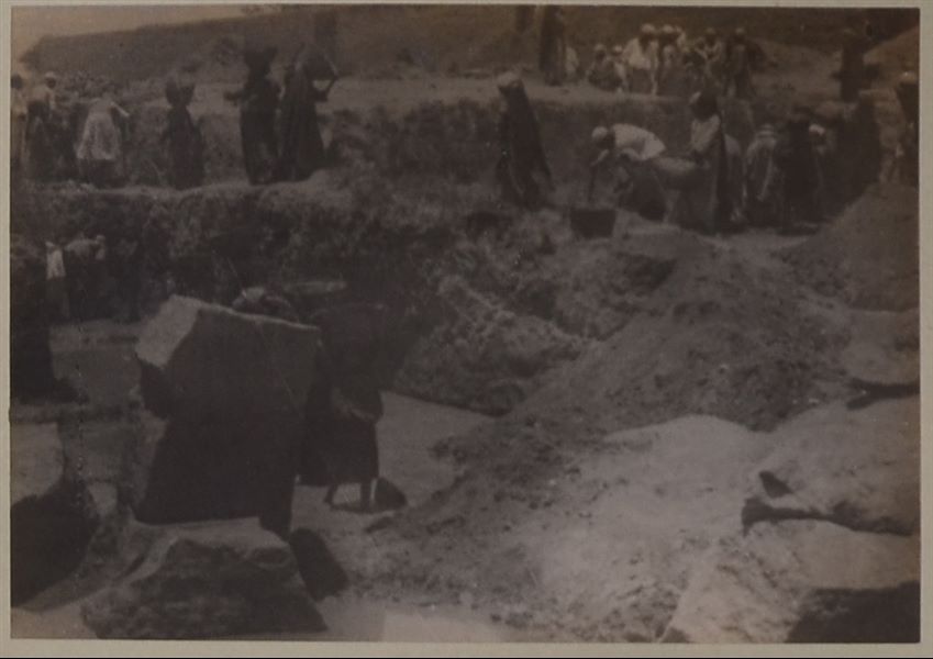 Temple of Mnevis, trench with fragments of the naos of Psamtik I. Note the muddy ground due to the presence of groundwater that has compromised the preservation of the non-stone material. This paper print has been toned with sepia. Schiaparelli excavations.