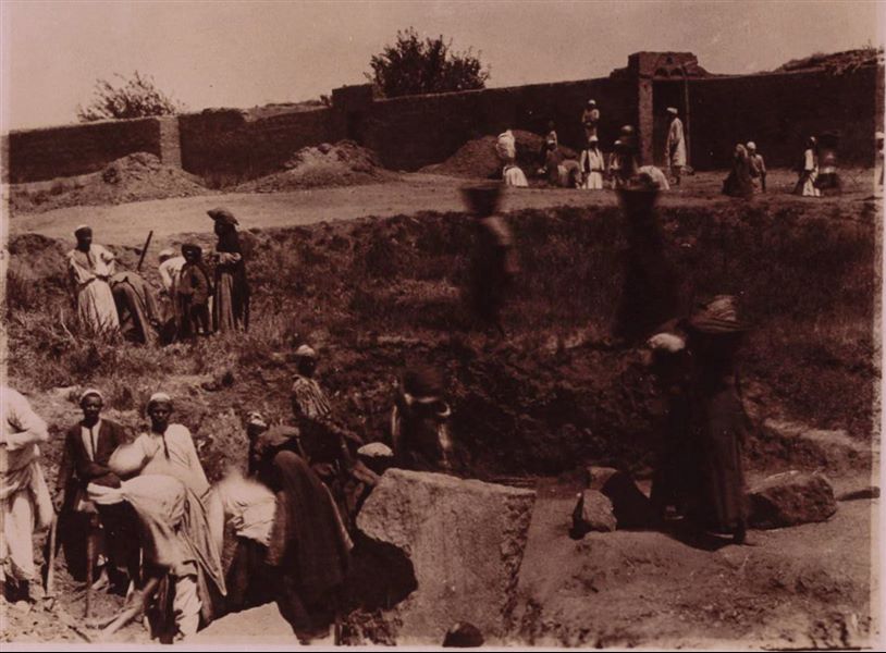 Tempio di Mnevis, trincea con frammenti del naos di Psammetico, a ridosso delle abitazioni. Da notare il terreno fangoso. La stampa su carta è stata virata con il color seppia. Scavi Schiaparelli.