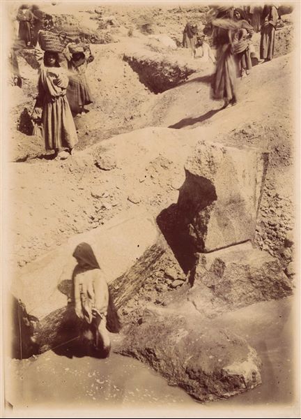 Temple of Mnevis, trench with fragments of the naos of Psamtik I. Note the muddy ground. This paper print has been toned with sepia.  Schiaparelli excavations. 