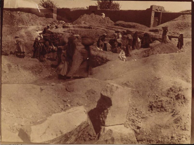 Temple of Mnevis, trench with fragments of the naos of Psamtik I, close to housing. Note the muddy ground. This paper print has been toned with sepia. Schiaparelli excavations.