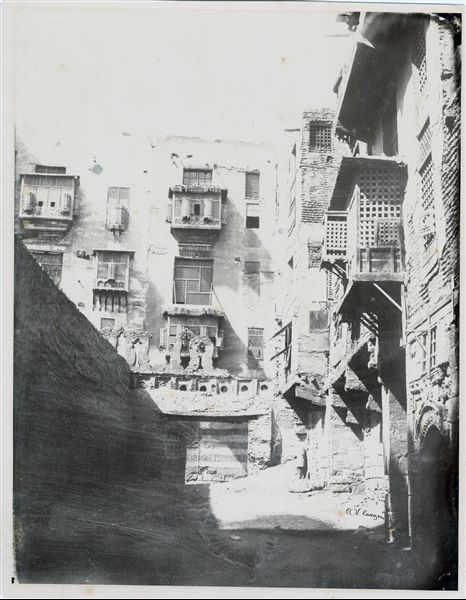 Particolare di un vicolo della città del Cairo, nel quale sono visibili le mashrabiyye, i caratteristici balconi chiusi con elaborate grate di legno. La firma dell’autore si trova in basso a destra.