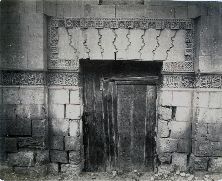 Particolare dell’ingresso decorato della tomba di Sadat el-Taulbe (da didascalia sul retro), che mostra il tipico stile ornamentale dell’arte islamica chiamato arabesco, oltre alla particolare composizione del portone di legno.