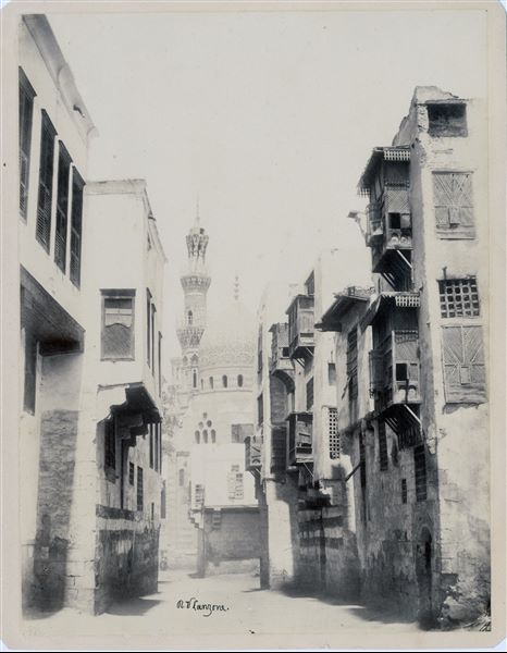 View of a street in Cairo, where the minarets of the Al-Rifa'i Mosque, which houses the mausoleum of part of Mohammed Ali's family and successors, including 20th century rulers including King Fuad I and King Farouk, can be seen. The author's signature is visible at the bottom right-hand corner. 