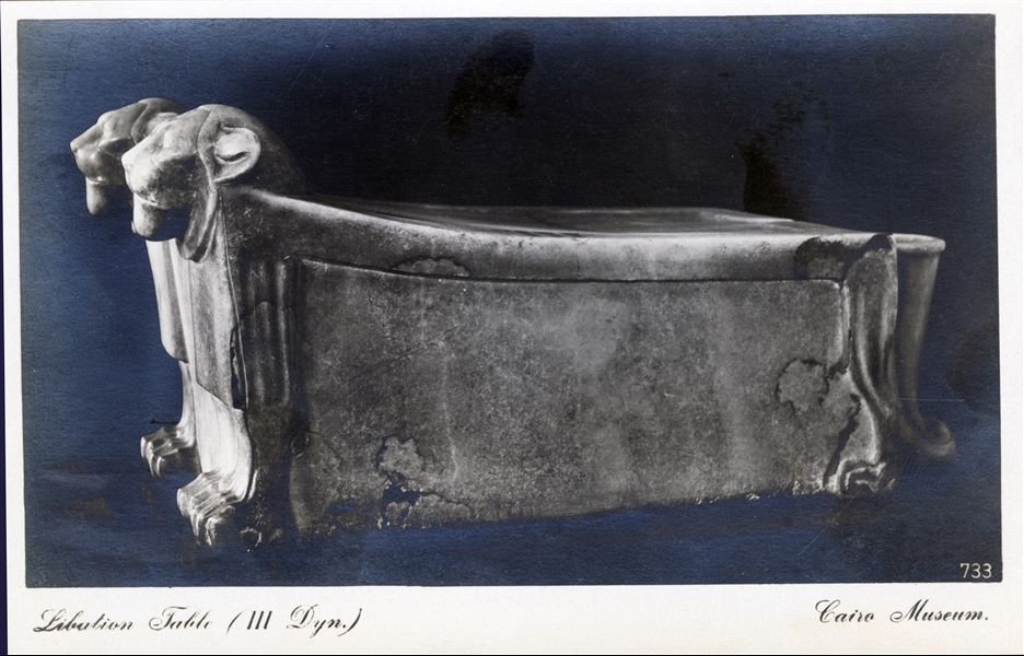 Gallery in the Egyptian Museum in Cairo. Particularly elaborate alabaster libation altar with two heads and eight lion paws. Datable to the 3rd dynasty. Album “Cartes postales” (Postcards).