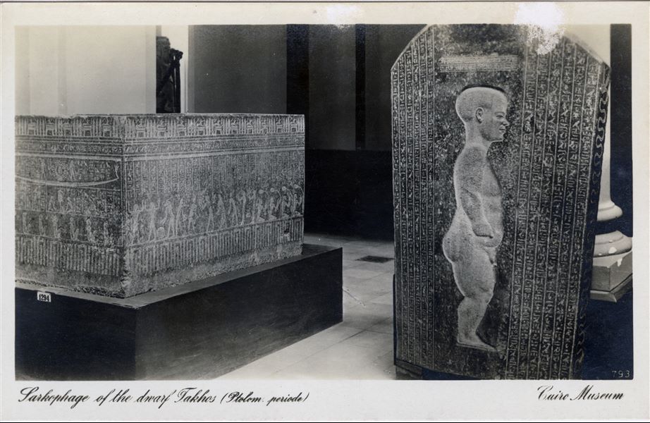 Gallery in the Egyptian Museum in Cairo. Granite sarcophagus of the dwarf Djeho, datable to the Late Period (30th dynasty). The text on the sarcophagus indicates that he worked as a dancer during ceremonies associated with the Apis bull cult. Album “Cartes postales” (Postcards).