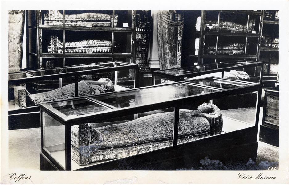 Gallery in the Egyptian Museum in Cairo. Arrangement of some coffins inside display cases. Album “Cartes postales” (Postcards).