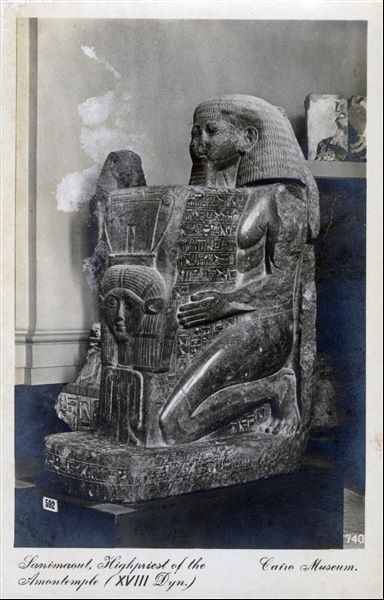 Gallery in the Egyptian Museum in Cairo. Statue of the architect and government official Senenmut, a very influential figure who lived during the reign of Queen Hatshepsut. He holds a shrine in front of him depicting the head of the goddess Hathor. The statue was found in Karnak. Album "Cartes postales" (Postcards).