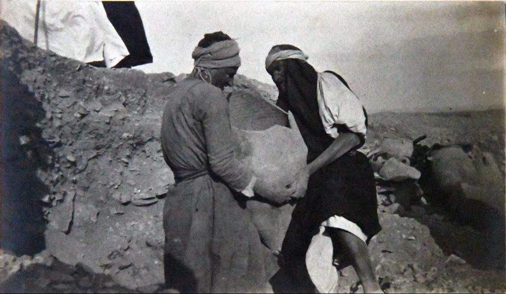 Photograph taken during excavations in the Giza necropolis in 1903, near the pyramid of Khufu and the surrounding necropolis. The image documents the discovery of a vase being lifted by two workers. Angelo Sesana Archive. 