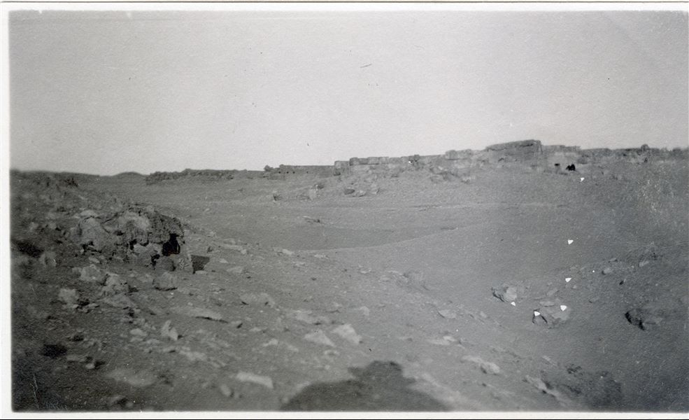 Photograph taken during excavations by the Italian Archaeological Mission in the Giza necropolis. The subject is unfortunately unidentifiable; a structure that should correspond to a mastaba tomb in the necropolis can be seen in the background, while the shadow of the photographer is clearly visible in the foreground. Schiaparelli excavations. 