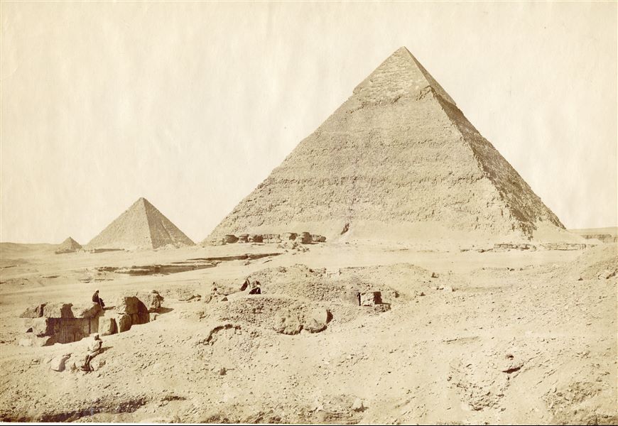Fotografia delle piramidi di Chefren (destra) e Micerino (sinistra), faraoni della IV Dinastia. In primo piano, alcuni abitanti locali in riposo. In basso a destra si trova la firma dell’autore.
