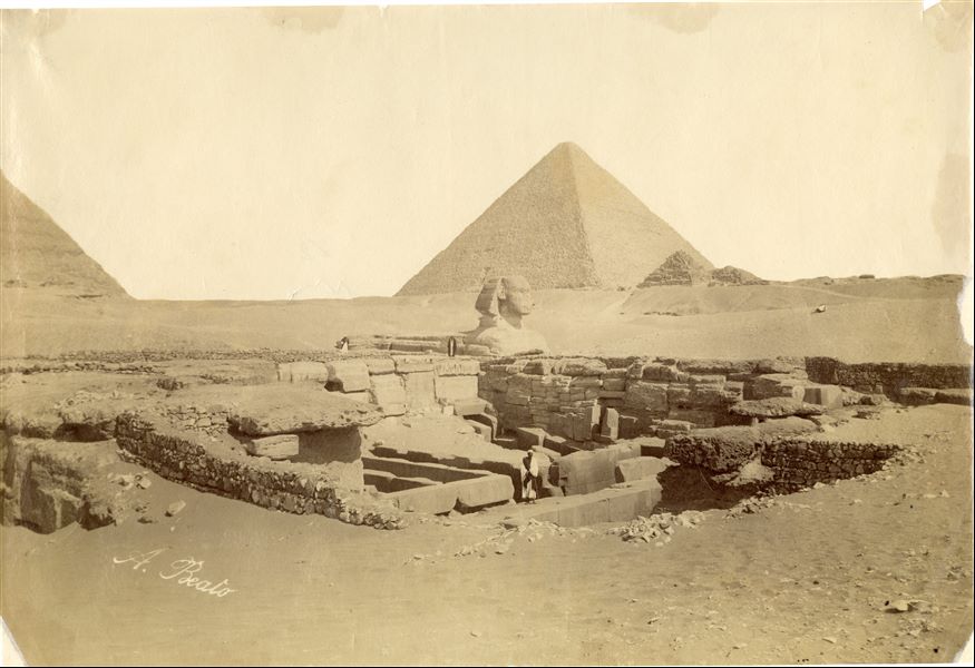 The photograph shows an overview of the monuments in the Giza Plateau, in particular the Pyramid of Khufu with satellite pyramids (in the background), the Valley Temple of Khafre (in the foreground) where part of the pyramid can also be seen on the left, and behind it is the Sphinx . The author's signature is clearly visible at the bottom left.  