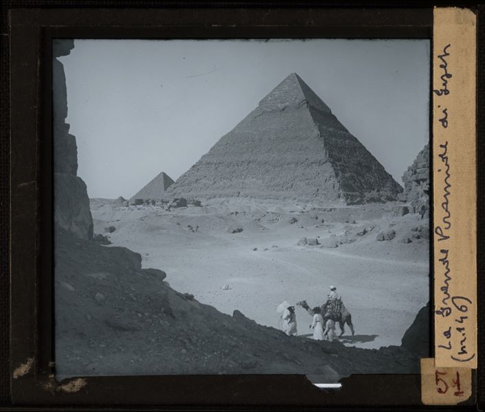 Some tourists with a camel in front of the pyramids of Giza. This is probably a 19th century photograph.