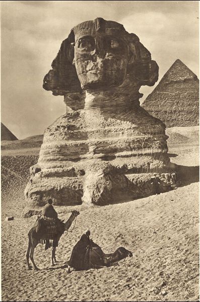 Front view of the Sphinx, not yet completely cleared of sand. In the background are two of the three major pyramids, that of Khafre on the right, and that of Menkaure on the left. 