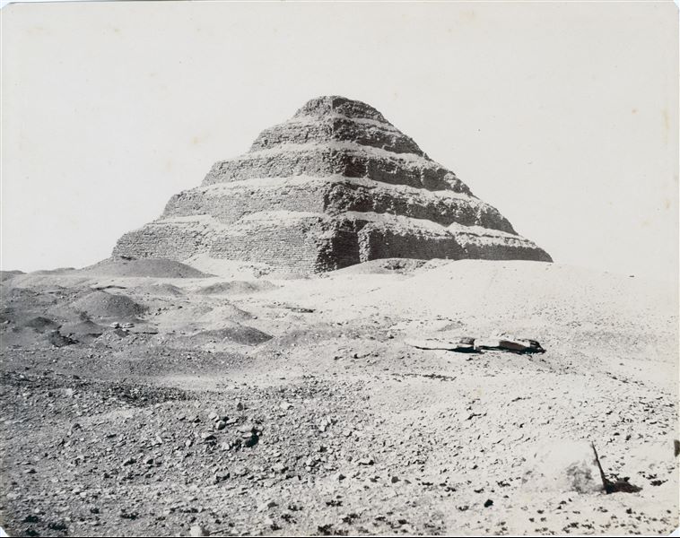 Fotografia della piramide a gradoni di Djoser, primo faraone della III Dinastia, a Saqqara. Tutt'intorno, l'area deve ancora essere scavata. L’immagine risulta leggermente sfocata.