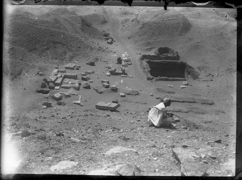 An Egyptian workman sitting in front of some ruins in the necropolis of Asyut. Schiaparelli excavations.