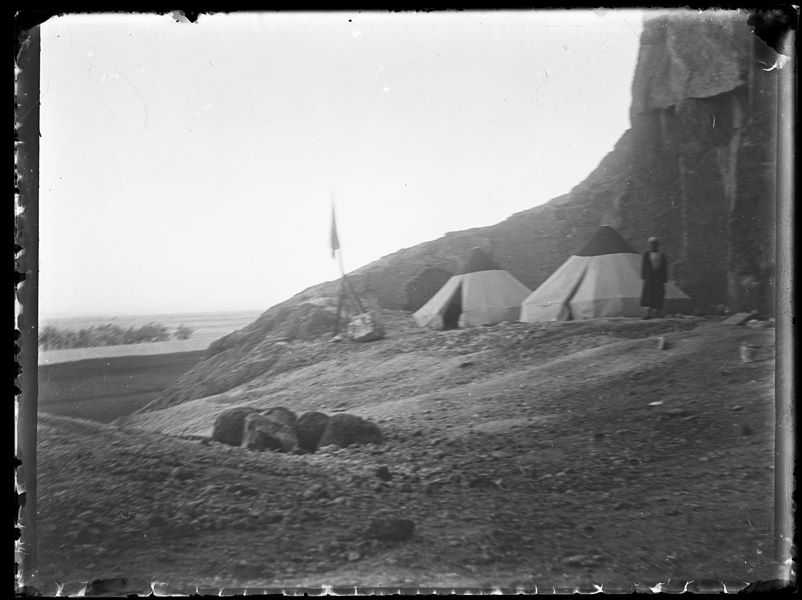  The Italian Archaeological Mission’s camp near the caves of Qau el-Kebir. Next to the tents and the flag, the cook Atallah can be seen standing. Schiaparelli excavations.