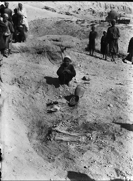 Excavation of a predynastic burial in the plain in front of  the rock-cut tombs. In the background, an Arab cemetery (from original label). Schiaparelli excavations.