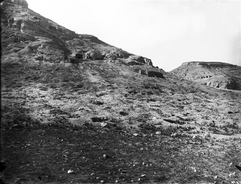 View of the rock-cut tombs, in the centre, the tomb of Wahka II. To the east (right), the so-called pylon followed by the chapel, and in the background the caves are visible. To the west (left) of the processional way, the remains of the so-called Greek tomb are recognisable. The photograph was presumably taken at the beginning of the excavation. Schiaparelli excavations.
