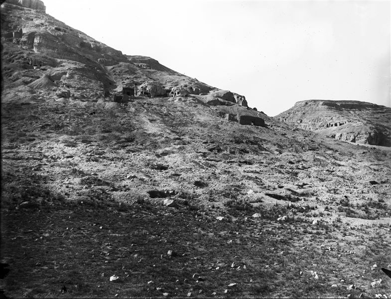 View of the rock-cut tombs, in the centre, the tomb of Wahka II. To the east (right), the so-called pylon followed by the chapel, and in the background the caves are visible. To the west (left) of the processional way, the remains of the so-called Greek tomb are recognisable. The photograph was presumably taken at the beginning of the excavation. Schiaparelli excavations.